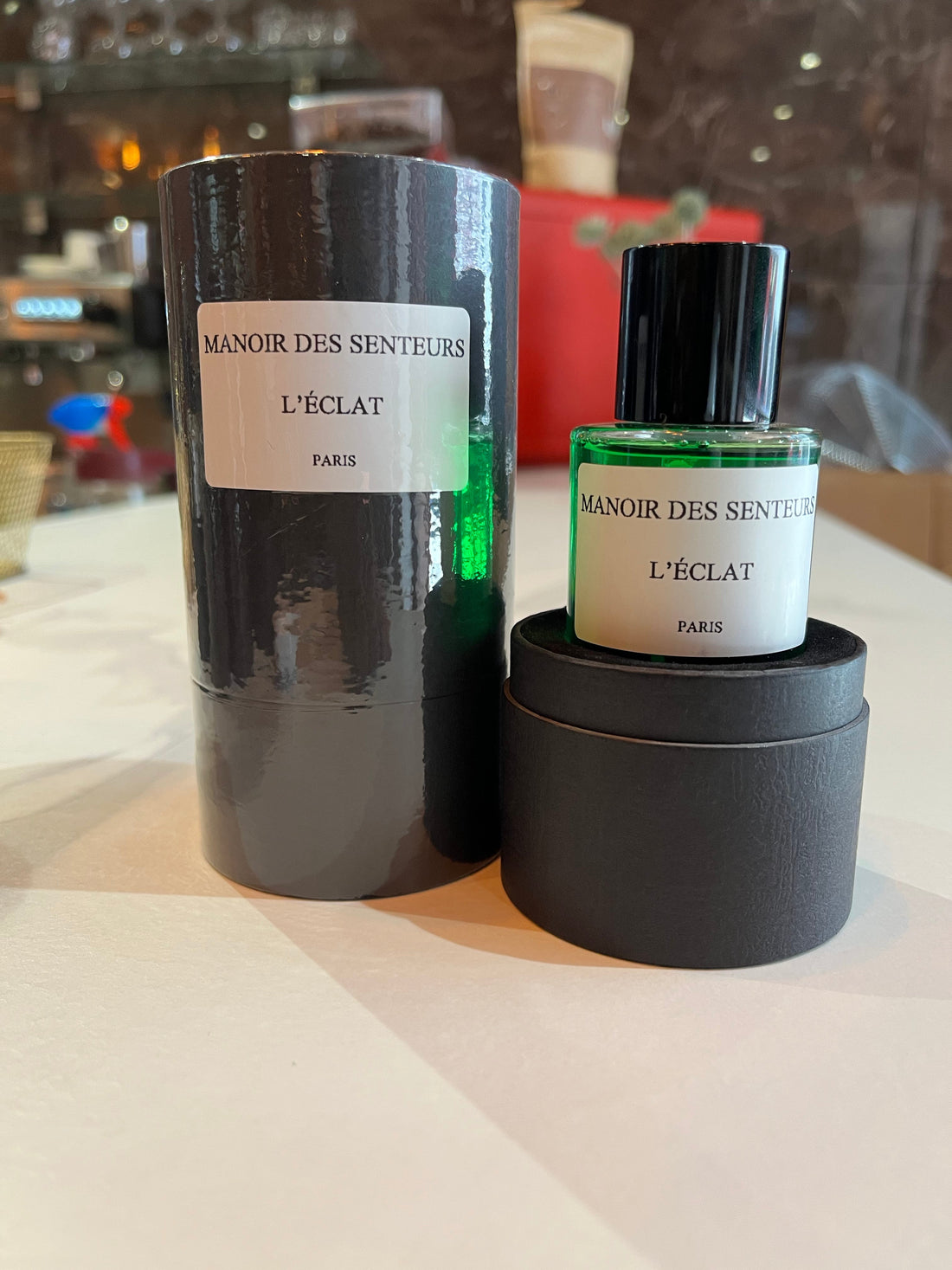 Flacon vert du parfum L'Éclat de Manoir des Senteurs Paris, accompagné de son coffret noir cylindrique.